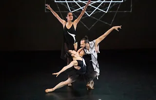 Three performers in black and white costumes mid-gesture on a dark stage