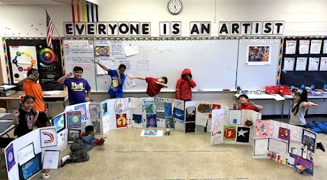 Young students presenting artwork boards beneath a banner reading Everyone Is An Artist